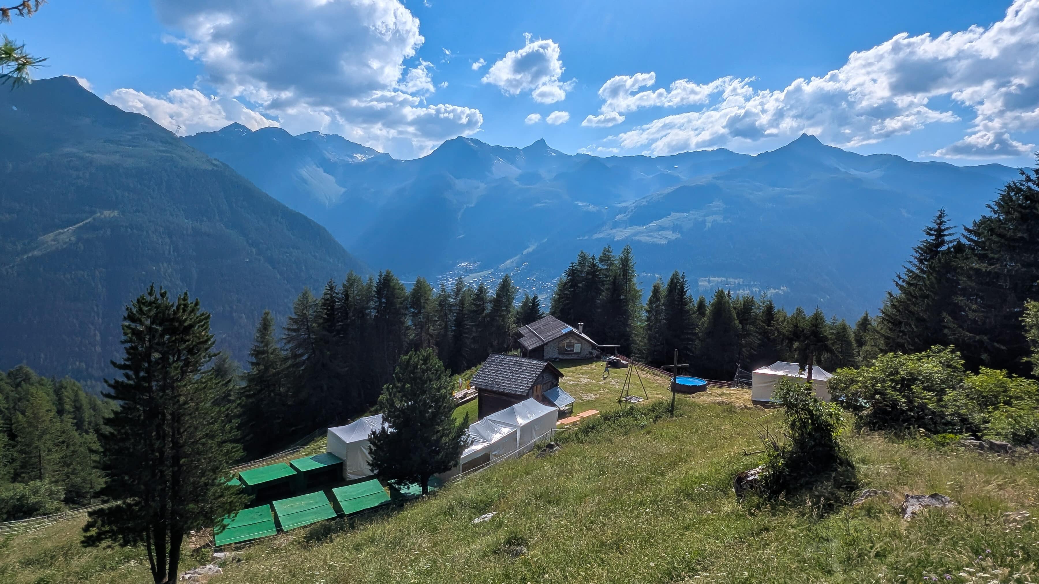 Paysage de montagne avec chalets, forêt et ciel nuageux.
