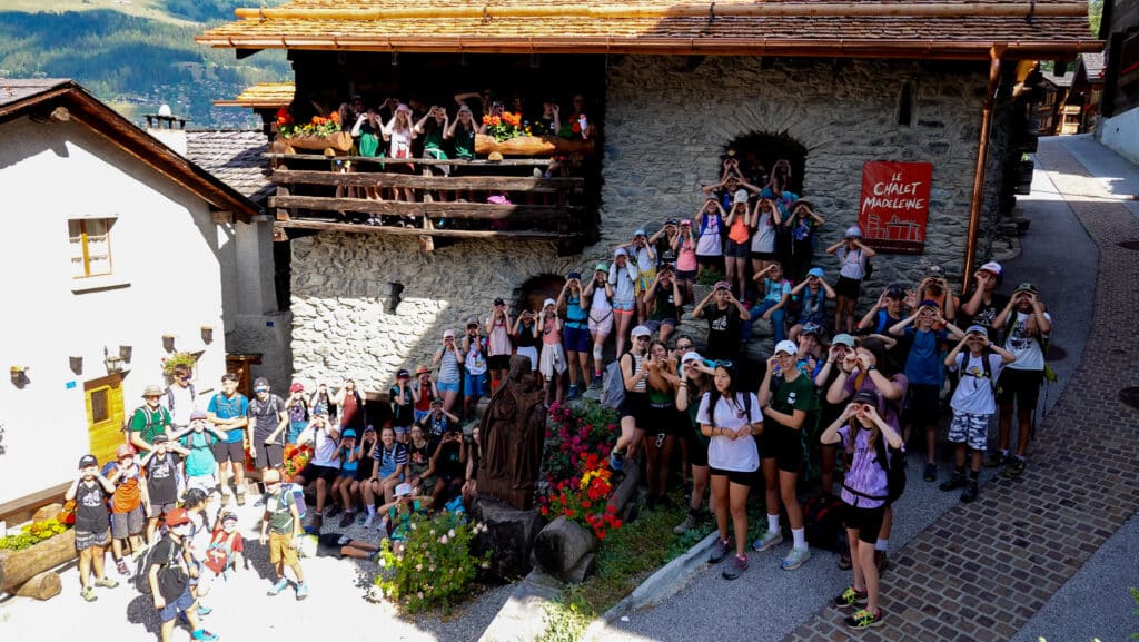 Grand groupe de jeunes posant devant un chalet de montagne.